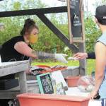 Lynsey Stow takes cash from customers at the opening day of the Homer Farmers Market while wearing personal protective gear on Saturday, May 30, 2020 in Homer, Alaska. (Photo by Megan Pacer/Homer News)