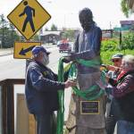 Mike Kennedy, left, Will Files, center, and Leo Vait, right, attach strapes to the Brother Asaiah statue on the deck of Cosmic Kitchen on Saturday, June 6, 2020, in Homer, Alaska. Vait created the statue as a commission by John Nazarian, a friend of Asaiah Bates. Nazarian had loaned to the Pioneer Avenue restaurant the statue of the man who coined the phrase Cosmic Hamlet by the Sea to describe Homer. The statue was moved after Cosmic Kitchen owners Michelle Wilson and Sean Hogan sold their restaurant. Cosmic Kitchen closed on Saturday. The Asaiah statue will be stored until a new location can be found. (Photo by Michael Armstrong/Homer News)