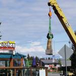 Mike Kennedy, in the crane at right, raises the Brother Asaiah statue from the deck of Cosmic Kitchen on Saturday, June 6, 2020, in Homer, Alaska. Leo Vait, left, on the deck, created the statue as a commission by John Nazarian, a friend of Asaiah Bates. Nazarian had loaned to the Pioneer Avenue restaurant the statue of the man who coined the phrase Cosmic Hamlet by the Sea to describe Homer. The statue was moved after Cosmic Kitchen owners Michelle Wilson and Sean Hogan sold their restaurant. Cosmic Kitchen closed on Saturday. The Asaiah statue will be stored until a new location can be found. (Photo by Michael Armstrong/Homer News)
