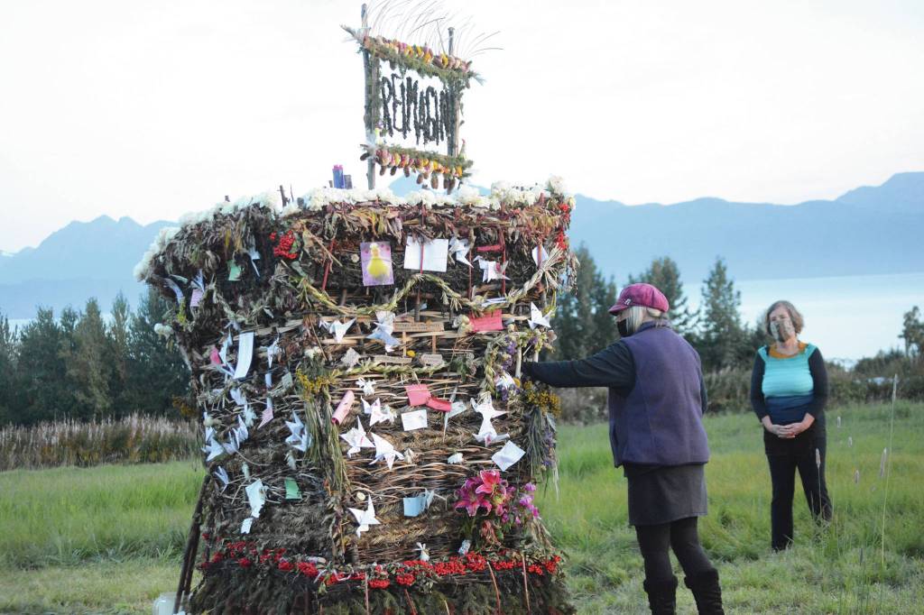 As Peggy Paver right, watches, Mavis Muller, left, places a note inReimagine, the 17th annual Burning Basket, in a field on Sunday, Sept. 13, near Homer. Artist and coordinator Muller intended to broadcast live on Facebook and YouTube the burning of the basket, but because of technical difficulties that didnt happen. Burning Basket teaches how to let go of expectations and accept the present moment, Muller wrote in a text message. Technology is fickle. The basket, however, did exactly what it promised to do. It helod our collective burderns, our memorials, our joys, sadness, fear, and dispersed all of our good intentions in a plume of smoke, sparks and flames. (Photo by Michael Armstrong/Homer News)