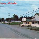 An undated postcard shows Pioneer Avenue looking west in Homer, Alaska, before it was paved. The building on the right is the former Homer Womens Club which later became the Homer News and then Cafe Cups. The remodeled building is now Little Mermaid Restaurant. The postcard is included in the museums Greetings from the Past: History in Postcards exhibit that opened Thursday, Oct. 22, 2020, in Homer, Alaska. (Photo courtesy Pratt Museum from its collection)