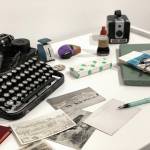 A display from the Pratt Museums Greetings from the Past: History in Postcards show old postcards, front, an address book, lower left, an Underwood typewriter, upper left, various office supplies, and a Kodak Brownie camera, upper right. The exhibit opened Thursday, Oct. 22, 2020, at the Pratt Museum in Homer, Alaska. (Photo courtesy Pratt Museum)