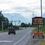 Cars pass the city of Homer advisory signs on Wednesday morning, June 24, 2020, at Mile 172 Sterling Highway near West Hill Road in Homer, Alaska. The sign also reads Keep COVID-19 out of Homer. (Photo by Michael Armstrong/Homer News)