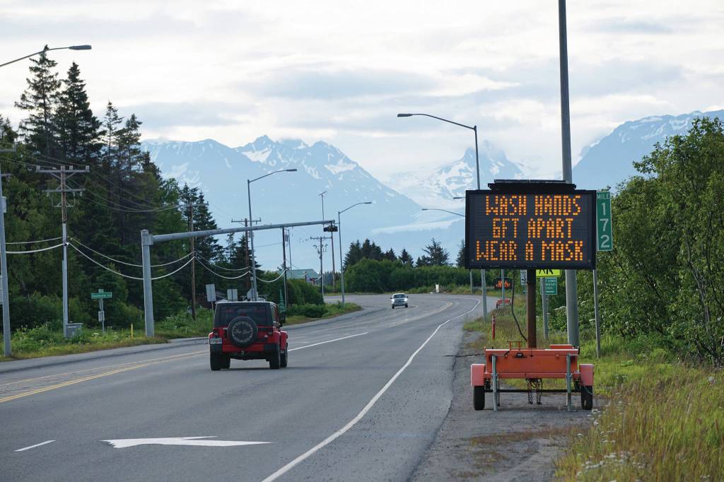 Cars pass the city of Homer advisory signs on Wednesday morning, June 24, 2020, at Mile 172 Sterling Highway near West Hill Road in Homer, Alaska. The sign also reads Keep COVID-19 out of Homer. (Photo by Michael Armstrong/Homer News)