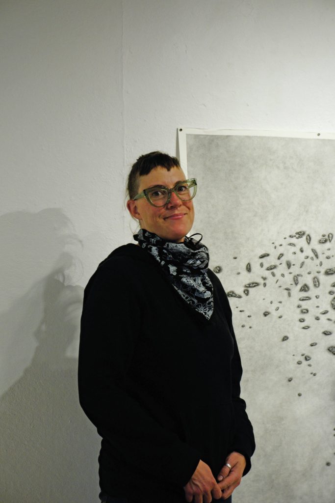 On Thursday, Feb. 11, 2021, in Homer, Alaska, Bunnell Street Arts Center Artist in Residence Nina Elder stands next to a drawing from her series, It Will Not Be the Same, But It Might Be Beautiful, drawings of puzzle stones collected in the area near McCarthy, Alaska. (Photo by Michael Armstrong/Homer News)