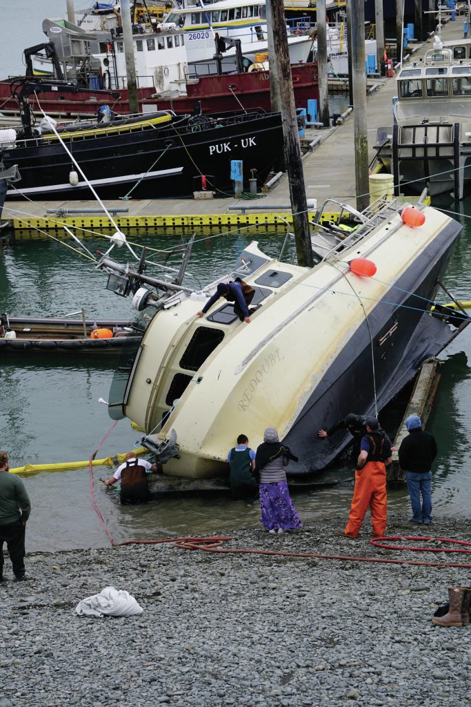 Workers respond to a fishing boat, the F/V Redoubt, that ran aground on the wooden grid on Wednesday, June 2, 2021, in the Homer Harbor in Homer, Alaska. The boat heeled over as the tide went out. (Photo by Michael Armstrong/Homer News)