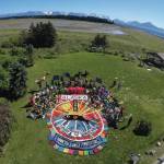 Homer’s Bishop’s Beach Park was the location for an enactment of public participatory art on Sunday, Aug. 1, 2021, in Homer, Alaska. A ground design of colored fabric was created to convey a message of “Alaska United,” “Teamwork Makes the Dream Work” and “Thank You Water Protectors.” The public was invited to be part of the art by standing and sitting around the central design. Salmon sculptures, raven and sandhill crane puppets, Alaska flags and colored bandanas were an added touch to the overhead image depicting salmon solidarity.  The project was led by Mavis Muller and was the finale to her series of 12 annual aerial group photos for the protection of Alaska’s Bristol Bay. Photographer Russell Campbell captured the photo from a bucket lift at 35 feet high.
“Art is communication. With our creativity and imagination we can inspire new possibilities, and we can have fun doing it,” Muller said. (Photograph by Russell Campbell)