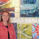 Tracy Hansen poses for a photo in front of her paintings at her Ocean Drive shop, 59 North, on Tuesday, Aug. 10, 2021, in Homer, Alaska. (Photo by Michael Armstrong/Homer News)