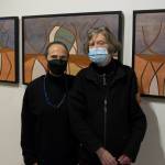 Rika Mouw and Turid Senungetuk, wife of Ron Senungetuk, stand in front of Ron Senungetuk's artworks titled "Reindeer Herd I, II, III" during the exhibit's opening reception at the Pratt Museum and Park. (Photo by Sarah Knapp/Homer News)