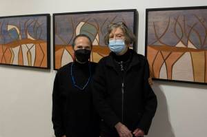 Rika Mouw and Turid Senungetuk, wife of Ron Senungetuk, stand in front of Ron Senungetuk's artworks titled "Reindeer Herd I, II, III" during the exhibit's opening reception at the Pratt Museum and Park. (Photo by Sarah Knapp/Homer News)