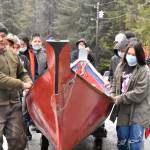 Tlingit master carver Wayne Price, left, and students from Angoon High School wheel a dugout canoe down to the Angoon waterfront on Tuesday, Oct. 26, 2021, for a ceremony commemorating the bombardment of the village by the U.S. Navy in 1882. Dugout canoes were specifically targeted by the navy for destruction, and Price said crafting a new one was a way of healing from the past. (Peter Segall / Juneau Empire)