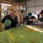 Bench creator, Brad Hughes, pours the molding material over the clay while Rob Wiard and Matt brush the liquid rubber over each character on the bench to ensure it is covered evenly. (Photo by Sarah Knapp/Homer News)