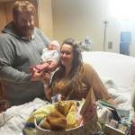 Jacob Fraley, left, holds his new daughter, Betty Lynn Fraley, while mother Cassy Quinlan, right,  watches on Wednesday, Jan. 19, 2022, at South Peninsula Hospital in Homer, Alaska. Betty Lynn was born on Jan. 17, 2022, the first baby of the New Year. Some of the gifts the family received for having the first baby of the year are in front of Quinlan. (Photo courtesy of South Peninsula Hospital)