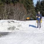 Kachemak Nordic Ski Club volunteer Roy Wilson, left, watches the final Kachemak Marathon skier, Kevin Walker, right, cross a snow bridge over Diamond Ridge Road on Saturday, March 19, 2022, in Homer, Alaska. (Photo by Michael Armstrong/Homer News)