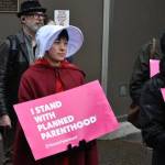 Lisa Denny wears "Handmaid's Tale"-inspired garb while holding a sign stating "I stand with Planned Parenthood" during a protest held near the Alaska State Capitol on Tuesday, May 3, following a leaked draft of a Supreme Court decision that would overturn the landmark case Roe v. Wade. (Peter Segall / Juneau Empire)