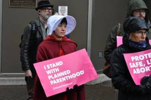 Lisa Denny wears "Handmaid's Tale"-inspired garb while holding a sign stating "I stand with Planned Parenthood" during a protest held near the Alaska State Capitol on Tuesday, May 3, following a leaked draft of a Supreme Court decision that would overturn the landmark case Roe v. Wade. (Peter Segall / Juneau Empire)