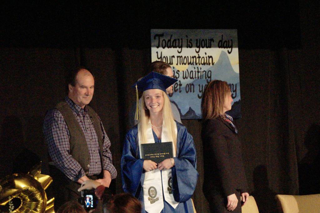Ava Halstead walks at Homer High School graduation exercises in the Alice Witte Gymnasium for commencement on Wednesday, May 18, 2022, at Homer High School in Homer, Alaska. At left is Kenai Peninsula School Board member Tim Daugharty. (Photo by Michael Armstrong/Homer News)