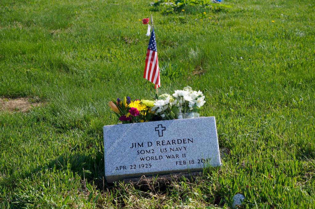 A U.S. flag and a poppy decorate the grave of Homer author and World War II veteran Jim Rearden at Memorial Day Ceremonies on Monday, May 30, 2022, at Hickerson Memorial Cemetery near Homer, Alaska. (Photo by Michael Armstrong/Homer News)