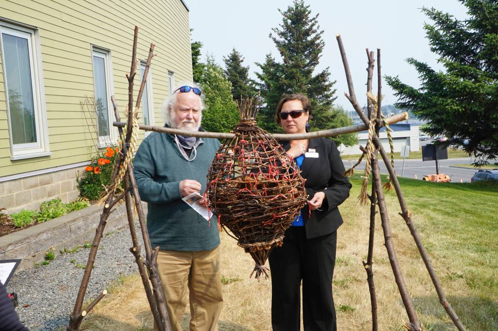 Pastor Lisa Talbott, right, of Homer United Methodist Church, and Joseph Talbott, left, place spruce cones in rememberance of Anesha Duffy in the Sphere of Love, a sculpture by Mavis Muller. Pastor Talbott delivered a prayer at the dedication of the Loved & Lost Memorial Bench on Sunday, June 12, 2022, at the Homer Public Library in Homer, Alaska. (Photo by Michael Armstrong/Homer News)