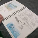 Ingrid Harrald looks at Kate Lochridge's sketch book at a pop-up viewing of her show on Friday, Aug. 5, 2022, at the Homer Council of the Arts in Homer, Alaska. (Photo by Michael Armstrong/Homer News)