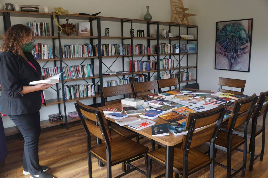 At an open house for the Storyknife Writers Retreat on Monday, Aug. 29, 2022, Storyknife board member Patty Stith looks at one of the books published by past Storyknife fellows in the library of Eva, the main house for the retreat near Homer, Alaska. (Photo by Michael Armstrong/Homer News)