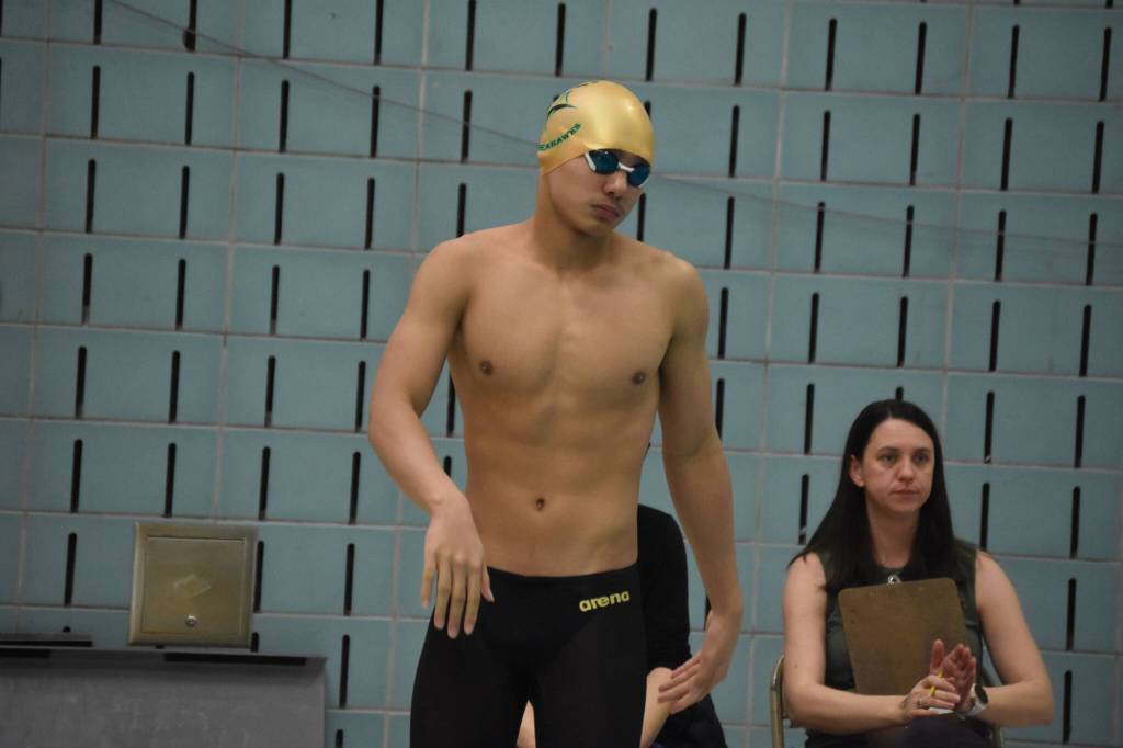 Nickolas Ambrosiani swings his arms to loosen up before swimming the 50-yard freestyle during finals at the ASAA State Swim & Dive Championships on Saturday, Nov. 5, 2022, at Bartlett High School in Anchorage, Alaska. (Jake Dye/Peninsula Clarion)