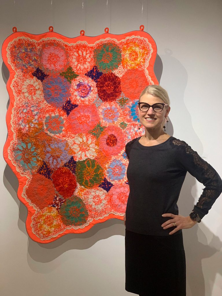 Amy Meissner poses with her work, Survival Blanket, at the opening of the Mother exhibit showing this month at Bunnell Street Arts Center. (Photo by Christina Whiting)