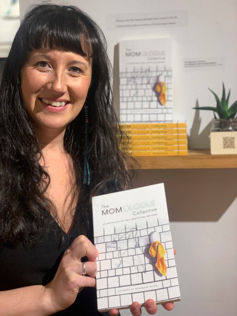 Brianna Allen poses with the book she edited, The MOMologues, at the opening of the Mother exhibit showing this month at Bunnell Street Arts Center. (Photo by Christina Whiting)