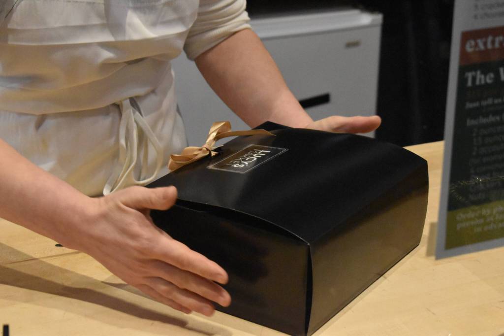 Kelsey Shields picks up a filled and sealed Cheese of the Month subscription box on Friday, Jan. 6, 2023 at Lucys Market in Soldotna, Alaska. (Jake Dye/Peninsula Clarion)