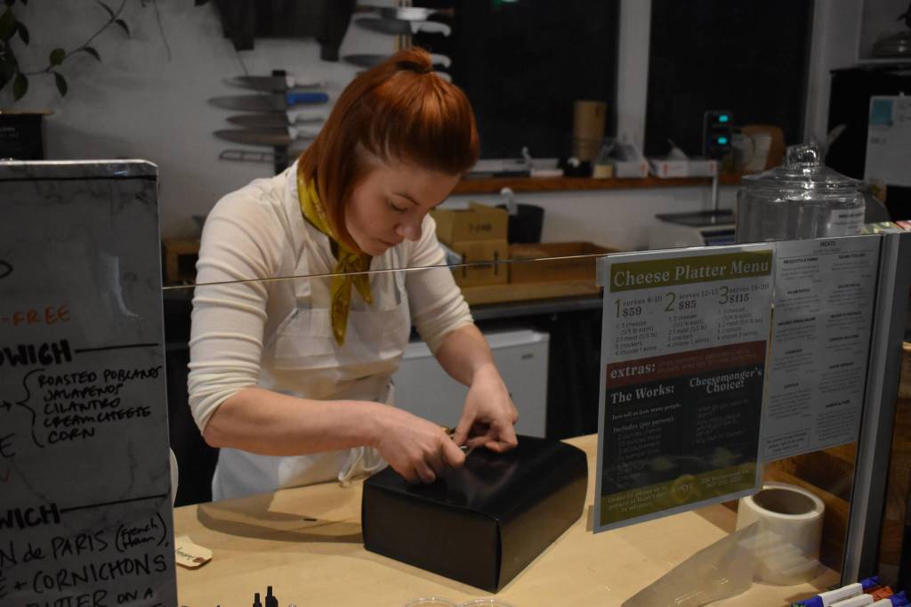 Kelsey Shields applies a Lucys Market sticker to a Cheese of the Month subscription box on Friday, Jan. 6, 2023 at Lucys Market in Soldotna, Alaska. (Jake Dye/Peninsula Clarion)