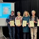 (from left to right) HCOA Community Arts awardees Daniel Perry (on screen), Michael Armstrong, Cathy Stingley, Krista Etzweiler, Sherry Stead and Brianna Allen pose with their awards at the HCOA annual meeting on Jan. 27, 2023, in Homer, Alaska.