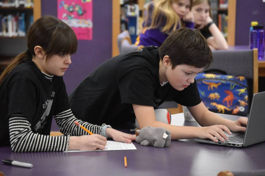 Emma Castimore and Andrew Stein communicate with their teammate Sawyer Graham, who used Zoom to participate from Texas, as they deliberate their response to a question posed during Kenai Peninsula Borough School District Middle School Battle of the Books competition on Thursday, Feb. 9, 2023, at Kenai Middle School in Kenai, Alaska. (Jake Dye/Peninsula Clarion)