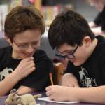 Luke Karpic and Oscar Marcou smile as they write their response to a question posed during Kenai Peninsula Borough School District Middle School Battle of the Books competition on Thursday, Feb. 9, 2023, at Kenai Middle School in Kenai, Alaska. (Jake Dye/Peninsula Clarion)