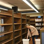 Homer High School librarian Deb Curtis checks trash cans staged near a row of empty bookshelves to catch water leaking from the ceiling on Tuesday, Feb. 21 in Homer, Alaska. Photo by Delcenia Cosman