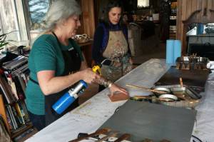 Ann-Margaret Wimmerstedt heats a plywood board for painting with encaustics on July 20, 2018 at Wimmerstedts home as artist Carla Klinker-Cope watches.