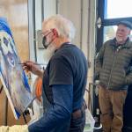 Potter Paul Dungan, right, looks on as Gary Lyons paints during the Ptarmigan Arts scholarship fundraiser at Grace Ridge Brewing on Saturday. (Photo by Christina Whiting/Homer News)