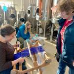 Janet Higley, right, looks on while Lisa Talbott weaves and Leah Dunn, rear center, paints during the Ptarmigan Arts scholarship fundraiser at Grace Ridge Brewing on Saturday. (Photo by Christina Whiting/Homer News)