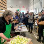 Lynn Naden (front left) paints scarves and Valisa Higman cuts paper during the Ptarmigan Arts scholarship fundraiser at Grace Ridge Brewing on Saturday. (Photo by Christina Whiting/Homer News)