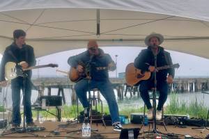 Homer youth musician Silas Jones performs on stage alongside U.S. military veteran musicians Shannon Book and Brandon Mills during the Homer Chamber of Commerce and Visitor's Center Summer Solstice Festival on Wednesday, June 21, 2023 at the Deep Water Dock n Homer, Alaska. Photo by Christina Whiting