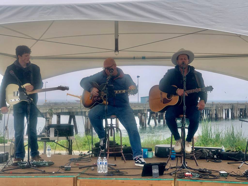 Homer youth musician Silas Jones performs on stage alongside U.S. military veteran musicians Shannon Book and Brandon Mills during the Homer Chamber of Commerce and Visitors Center Summer Solstice Festival on Wednesday, June 21, 2023 at the Deep Water Dock in Homer, Alaska. Photo by Christina Whiting