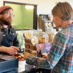 Jacob Chrisman, owner of Alasandros Market on Heath Street, discusses cheese with community member Heather Kallevig on Thursday, June 20, 2023 in Homer, Alaska. Photo by Christina Whiting