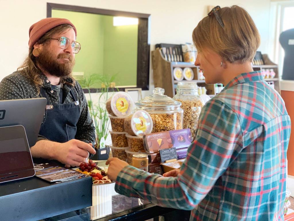 Jacob Chrisman, owner of Alasandros Market on Heath Street, discusses cheese with community member Heather Kallevig on Thursday, June 20, 2023 in Homer, Alaska. Photo by Christina Whiting
