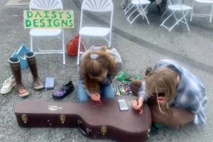 Daisy Walker (left) and her friend Leah Dunn paint a visiting musician's guitar case during the 2023 Solstice Festival on the Spit in Homer, Alaska. Photo by Christina Whiting