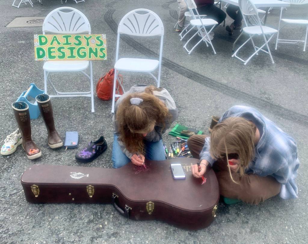 Daisy Walker (left) and her friend Leah Dunn paint a visiting musicians guitar case during the 2023 Solstice Festival on the Spit in Homer, Alaska. Photo by Christina Whiting