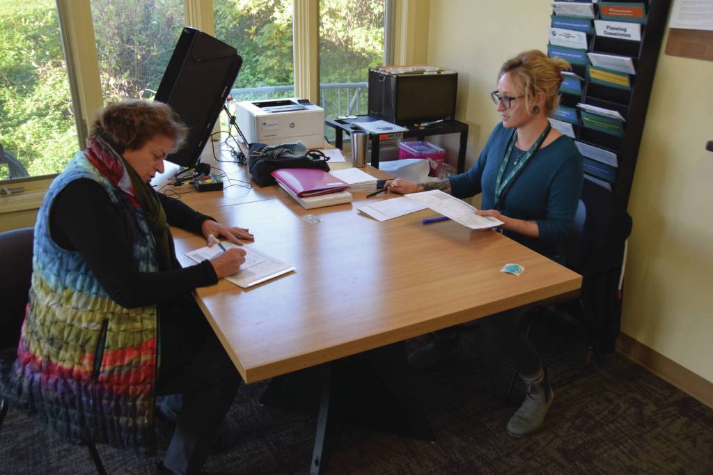 Rachel Tussey, election official with the City of Homer, helps a voter with registration before voting in the election on Tuesday Oct. 3. (Finn Heimbold/Homer News)