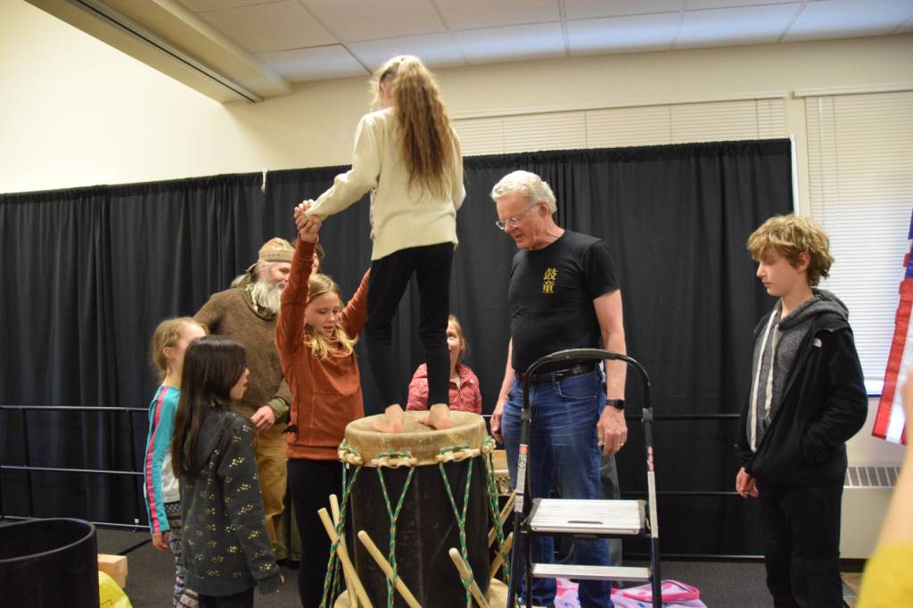 Margaret Gervais holds Yaella Bowman (center) steady while she jumps on top of the taiko drumskin in order to stretch it during the free workshop hosted at Kachemak Bay Campus on Friday, May 3, 2024 in Homer, Alaska. (Delcenia Cosman/Homer News)