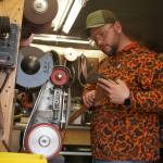 Grey Wilson, of Wilsons Proper Edge, examines the edge of an ax while sharpening it at Soldotna Creek Park in Soldotna, Alaska, on Wednesday, June 19, 2024. (Jake Dye/Peninsula Clarion)