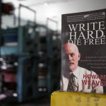 A copy of Howard Weavers memoir Write Hard, Die Free rests on an ink-splotched guard rail in front of the Peninsula Clarions defunct Goss Suburban printing press in Kenai, Alaska, on Thursday, June 20, 2024. (Jake Dye/Peninsula Clarion)