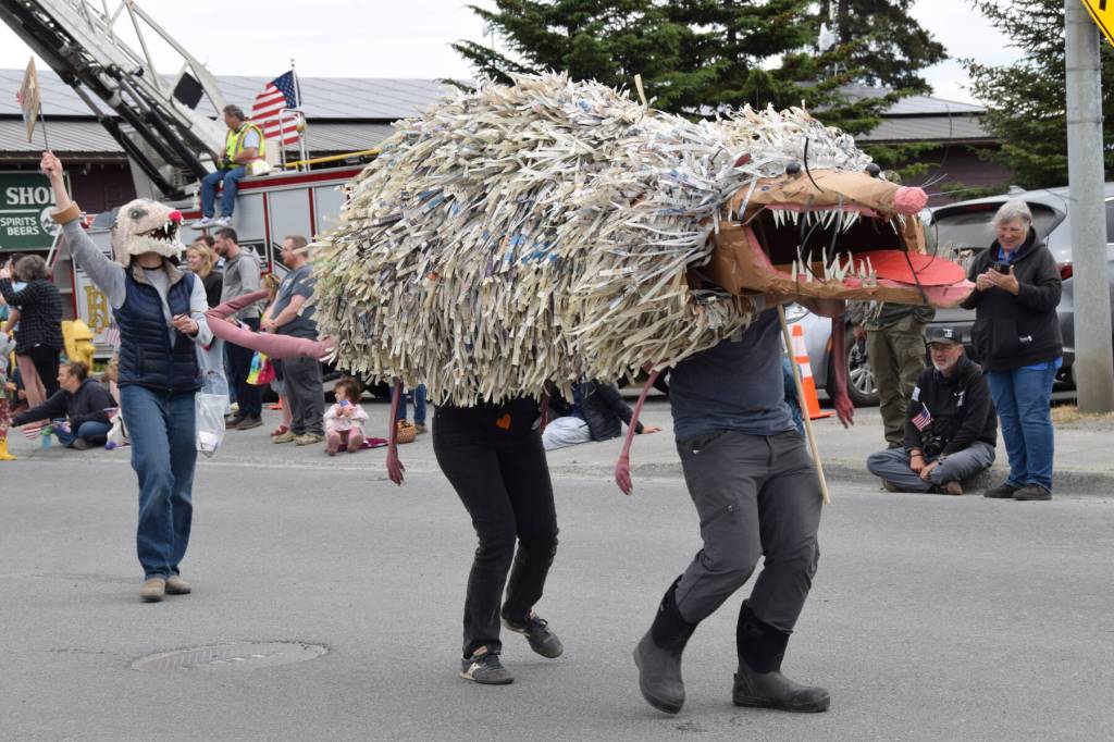 Bunnell Street Arts Center members participate in the Fourth of July parade with a wearable, walkable artwork of Grubby the Virginia opossum on Thursday, July 4, 2024, in Homer, Alaska. In the rear, a parade participant wearing an opossum mask waves a sign reading, Grubby for Prez. (Delcenia Cosman/Homer News)