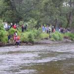 Spectators gather on the riverbank near the finish line during the third annual Anchor River Duck Races on Saturday, July 6, 2024, in Anchor Point, Alaska. (Delcenia Cosman/Homer News)